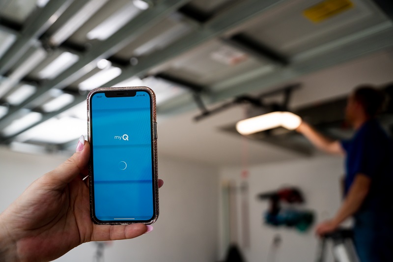 Cell phone with myQ app open and garage door opener technician in the background